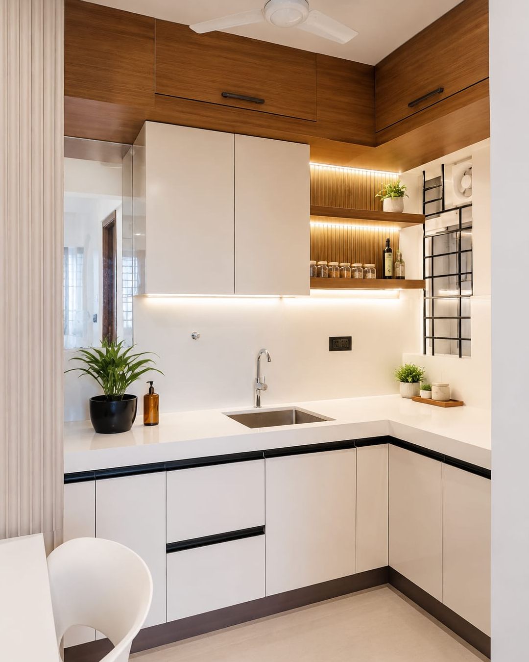Compact L-shaped kitchen in white handleless cabinetry with a stone counter, teak upper units and lit open shelving